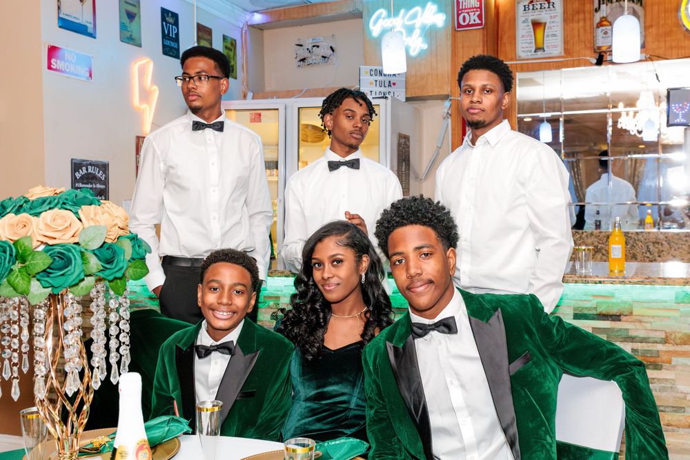 Family group photo with woman and four young men in formal green velvet and white tuxedos.