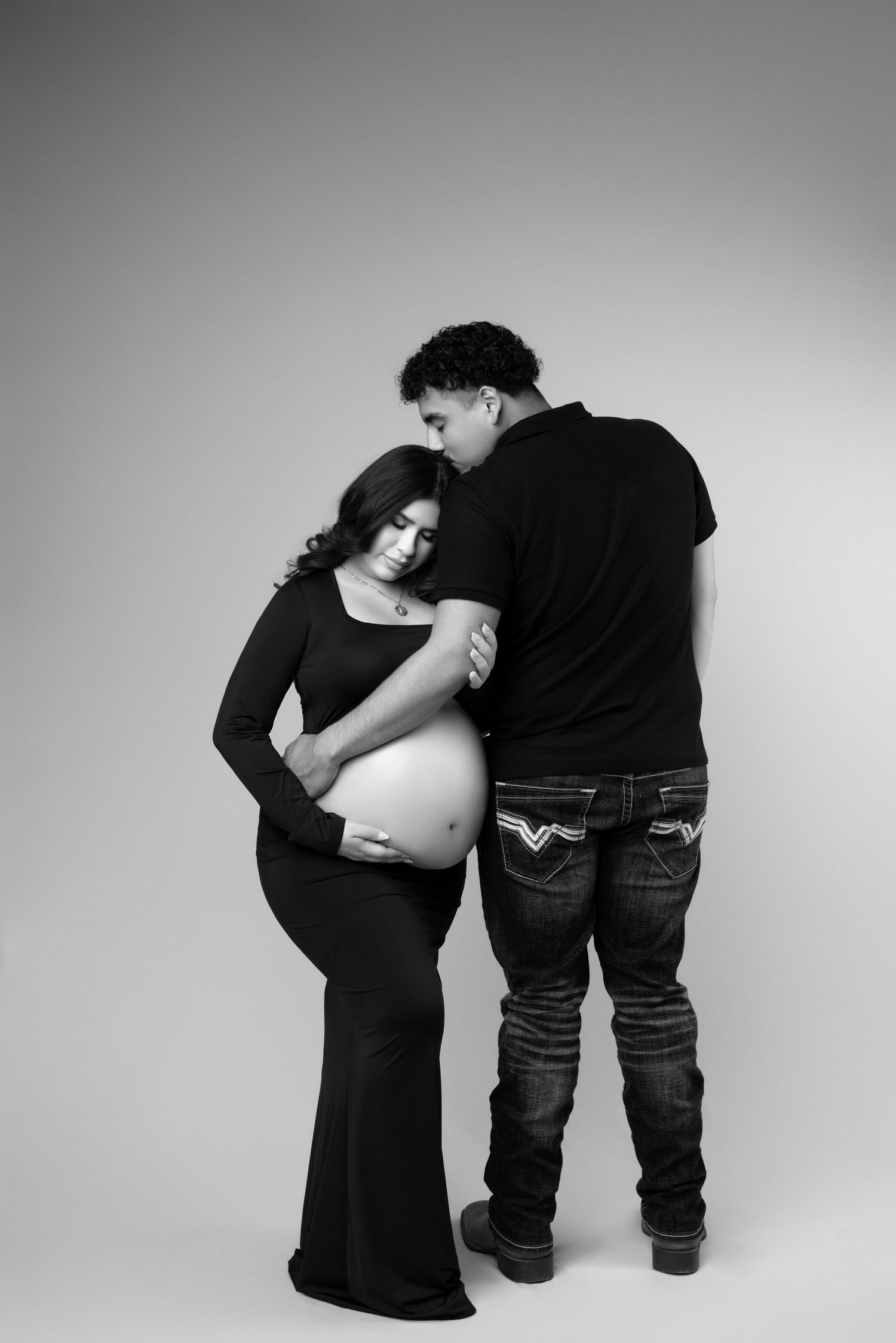 Intimate black and white maternity photo of couple embracing against simple background.