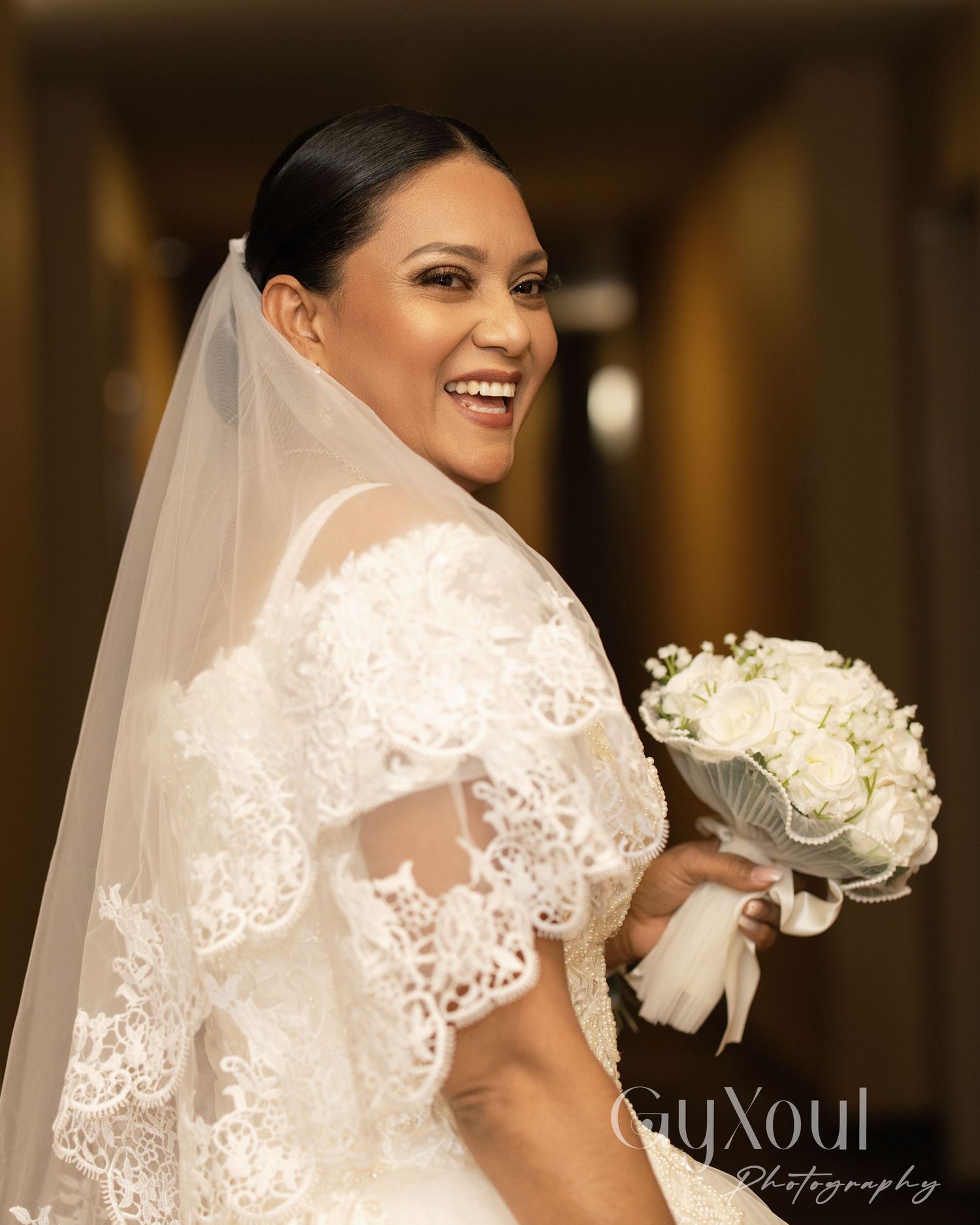 Side profile of bride in lace dress holding white rose bouquet.