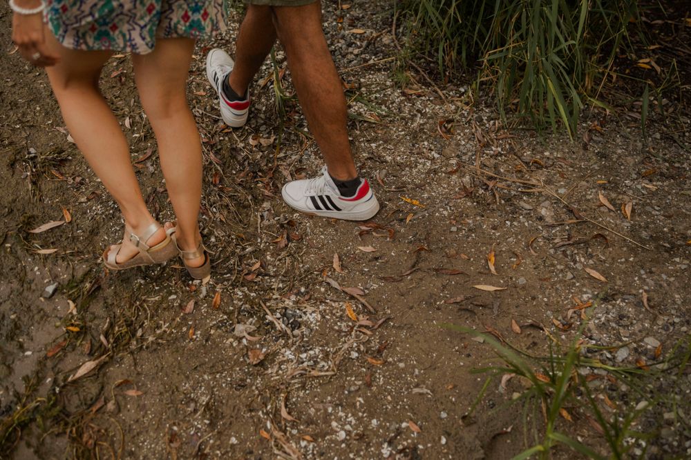 Couple walk on the shoreline of Lake Ontario. Kingston, On, Ca. Detail of their feet on the sandy ground covered in leaves.