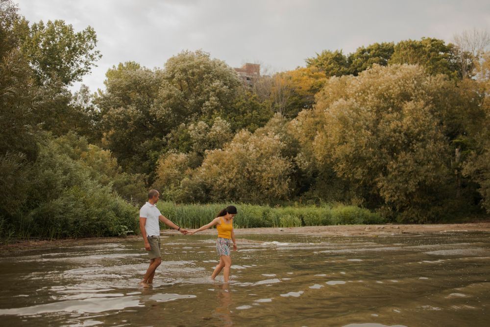 Couple walk along the shallow beach at Lake Ontario, . Wide shot with trees in the background.