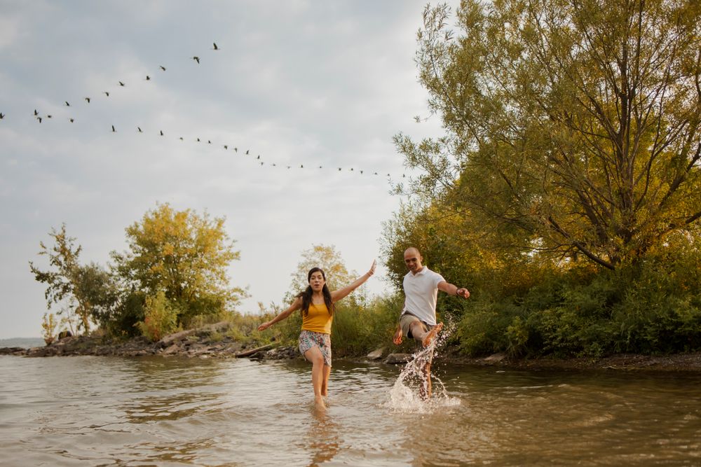 Couple splashes  in Lake Ontario, Kingston Ontario Canada. They laugh and smile. Canadian geese fly in formation above.