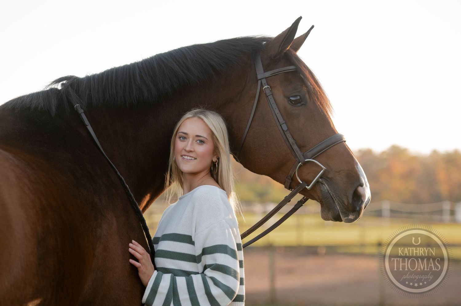 Autumn equestrian portrait features horse and companion in striped sweater against fall foliage.