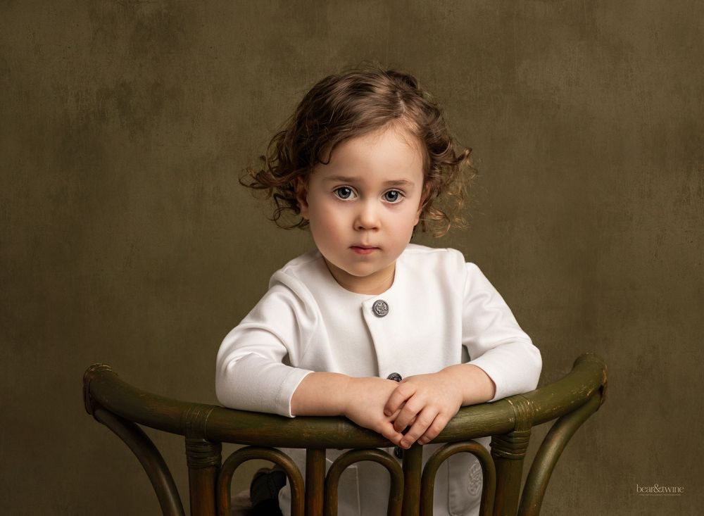 Fine art portrait of a boy on a green wicker chair.