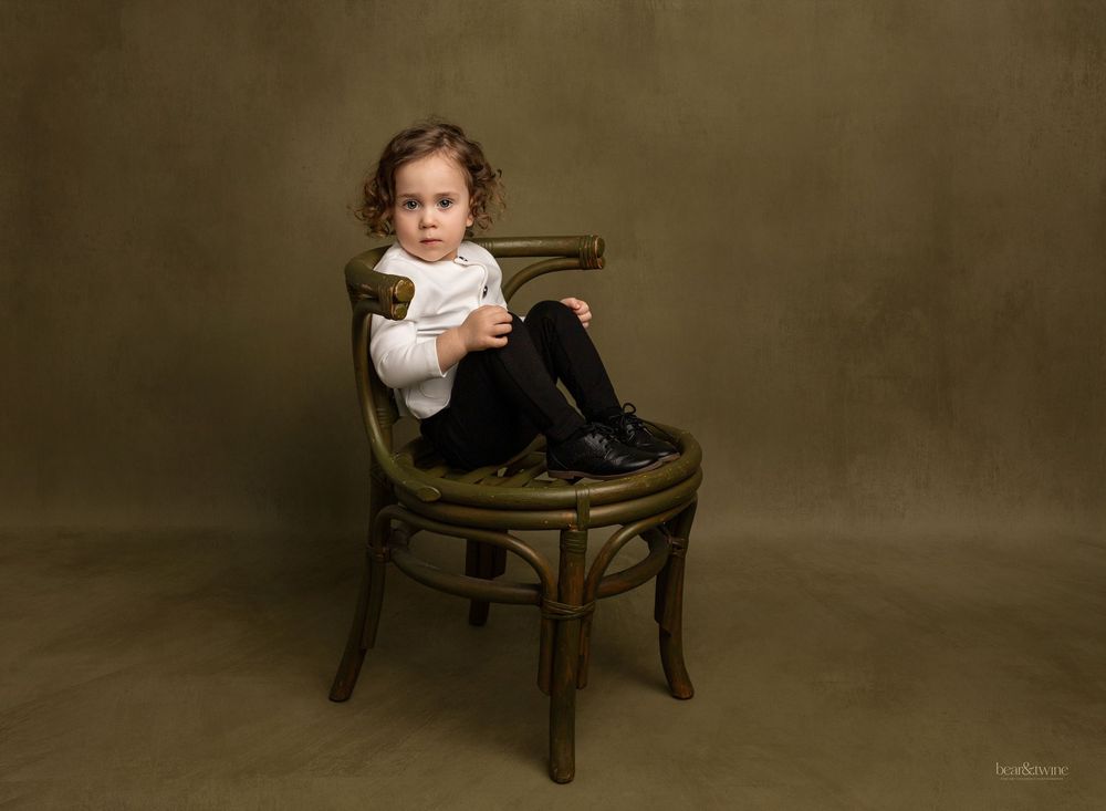 Fine art portrait of a boy sitting on a green wicker chair.