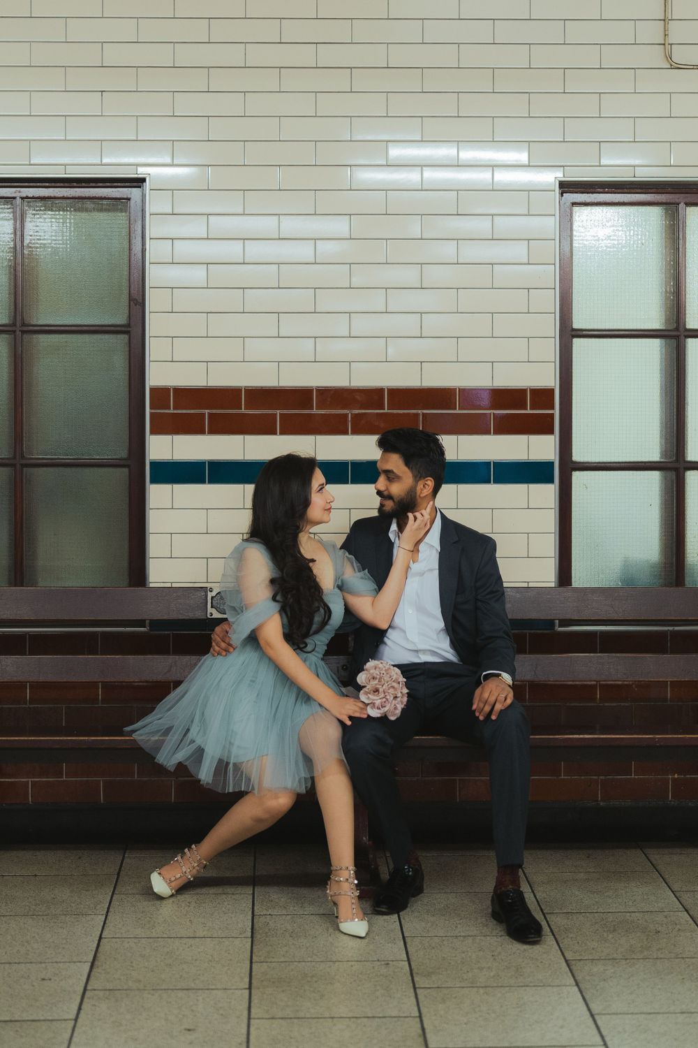 Couple sitting together on subway bench, woman in blue tulle dress touching mans face tenderly.