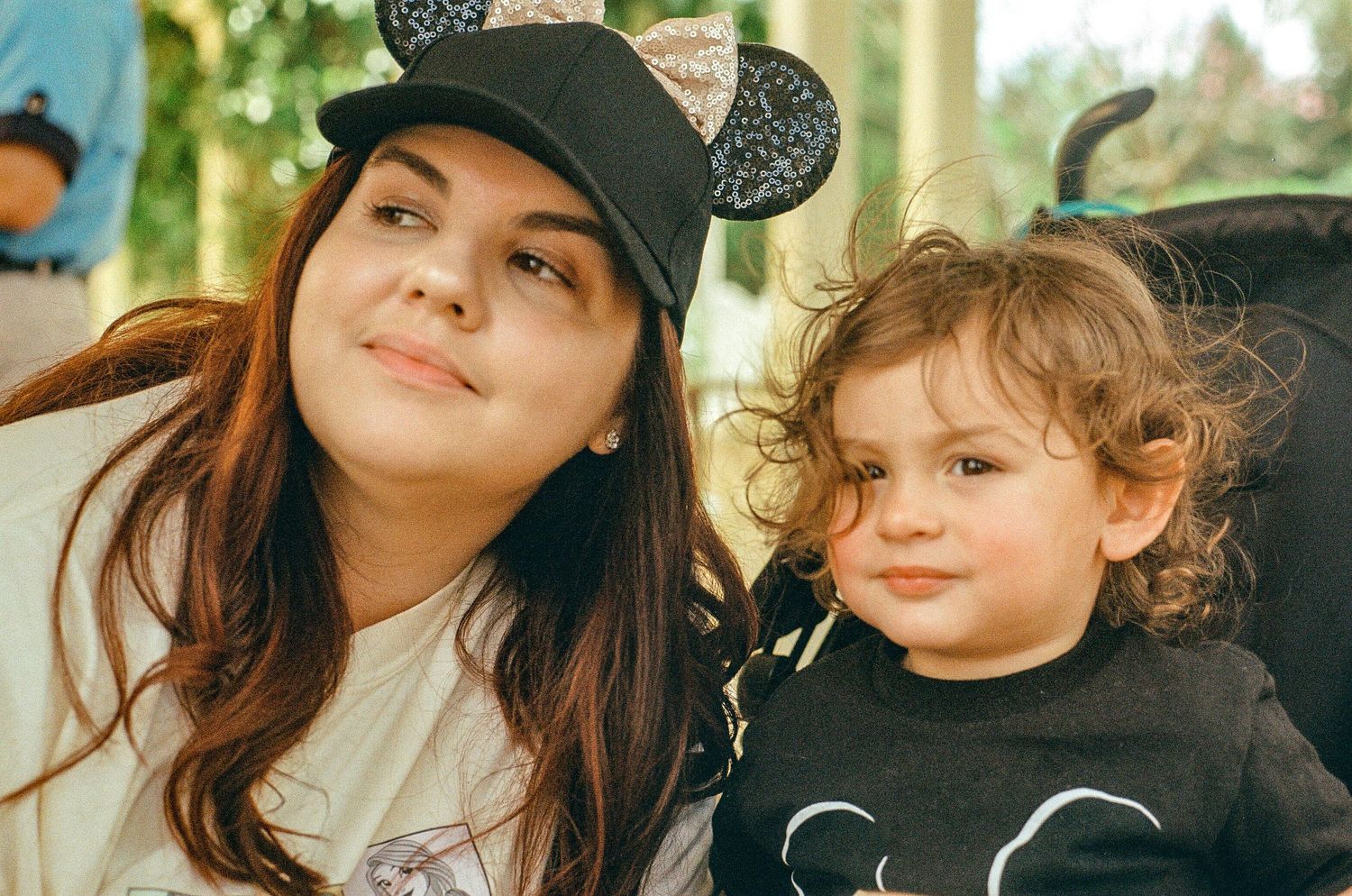 A parent and child wearing matching Mickey Mouse ear hats share a candid moment together outdoors.