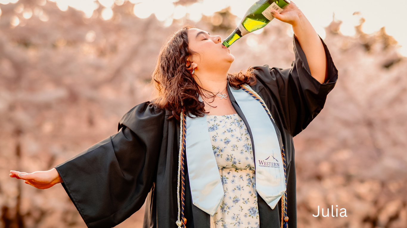 Graduate in black robe and stole celebrates by drinking from bottle outdoors.