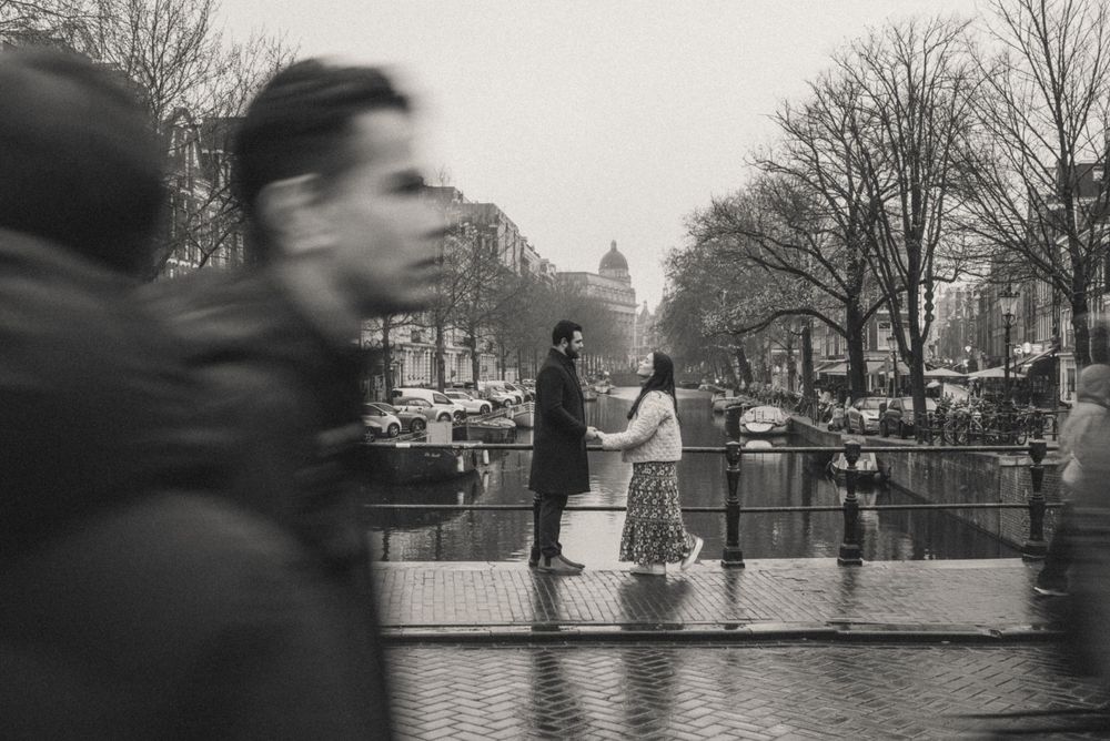 A black and white scene of people walking along an Amsterdam canal on a misty day.