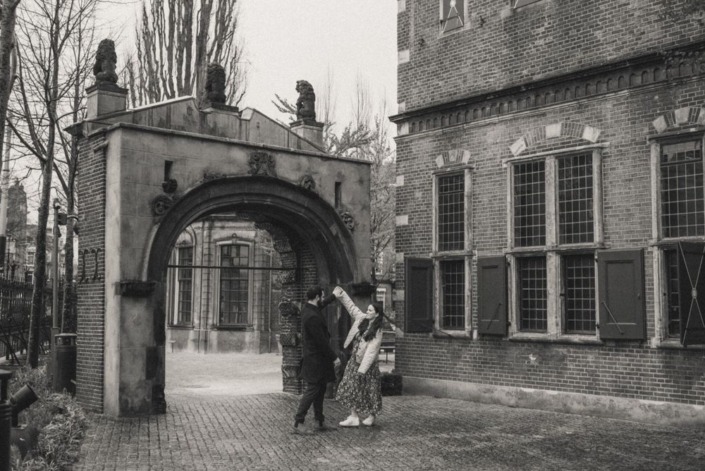 Historic brick buildings and archways line a quiet European street.