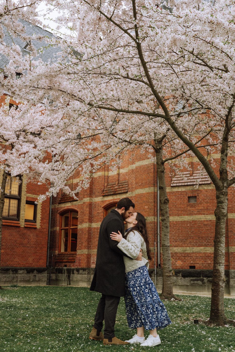 A tender moment captured under flowering cherry trees beside a brick building.