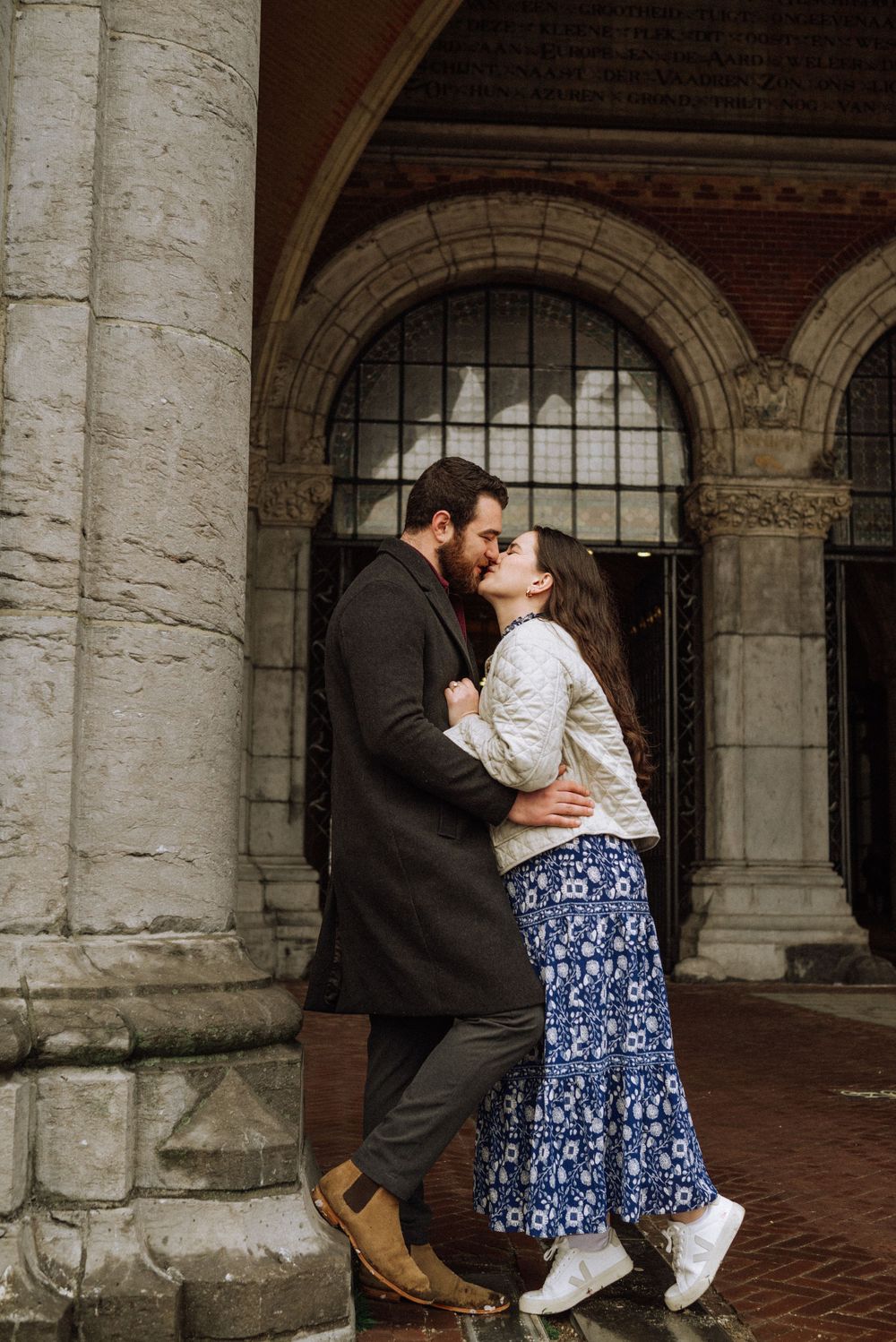 A romantic embrace between two people under stone archways of a historic building.