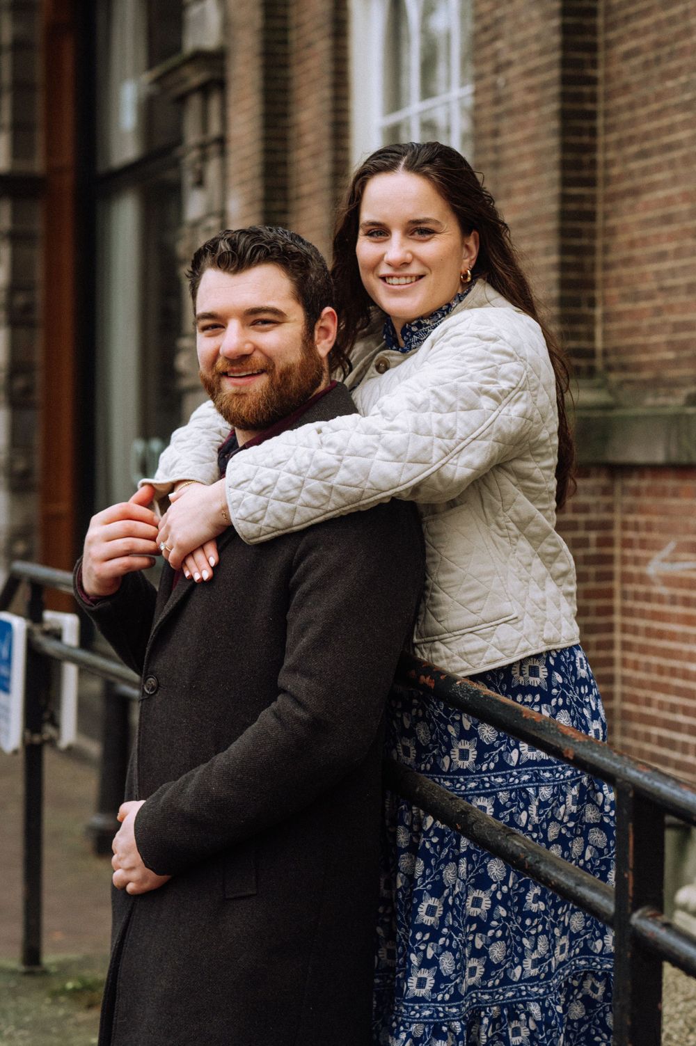 A couple leans against a railing while sharing a laugh together.