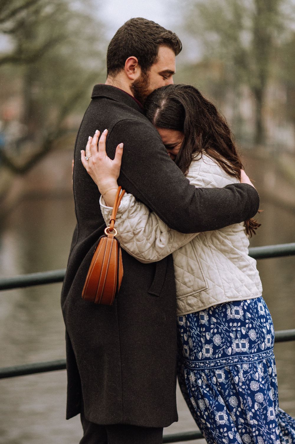Couple embracing on bridge in Amsterdam during overcast day.