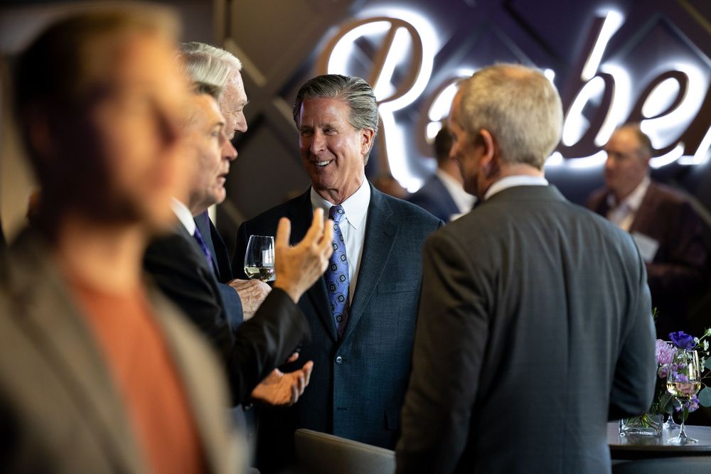 People in formal attire gather and socialize at an upscale event with dark lighting and elegant decor.