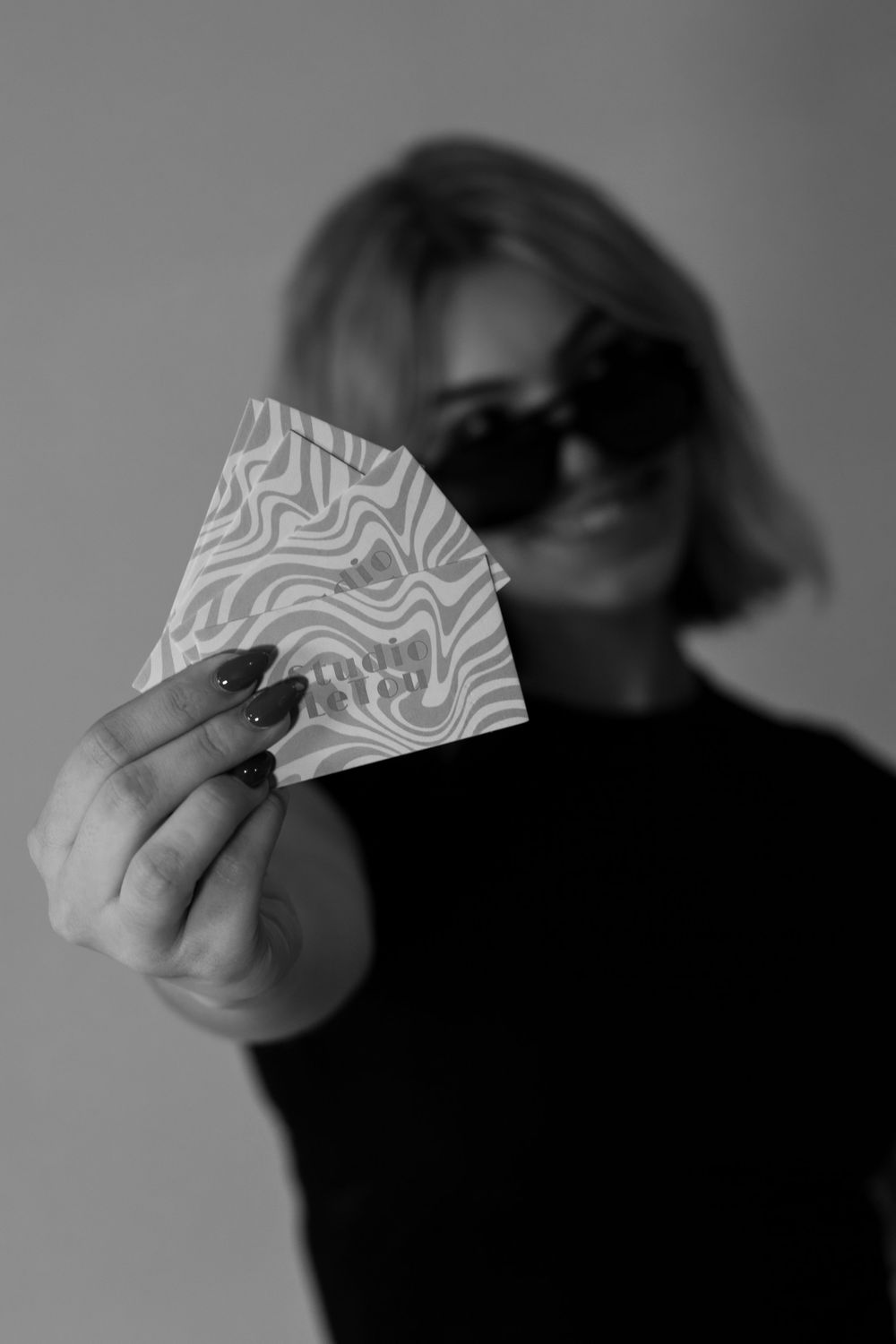 A blurred person in black holds up a wavy patterned paper fan against a monochrome background.