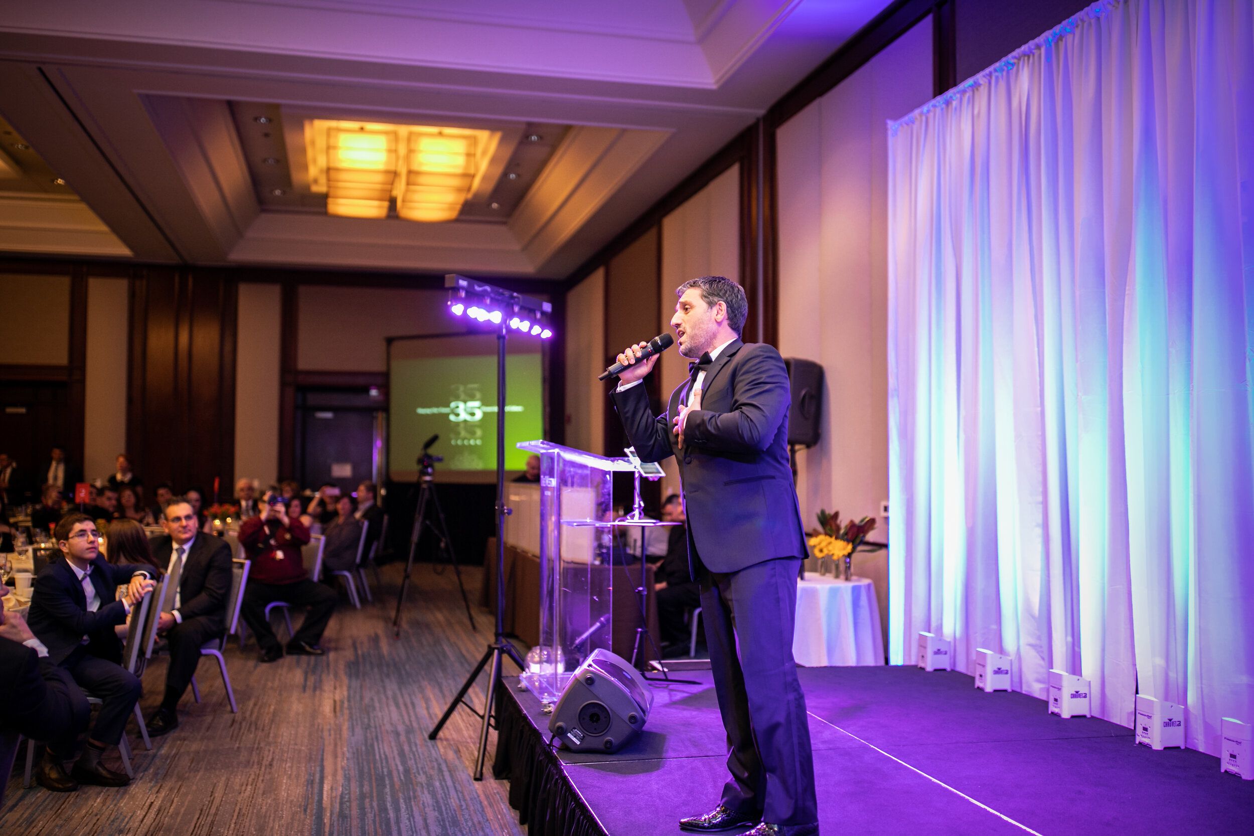 Man in suit performing on a stage at a fundraiser gala.