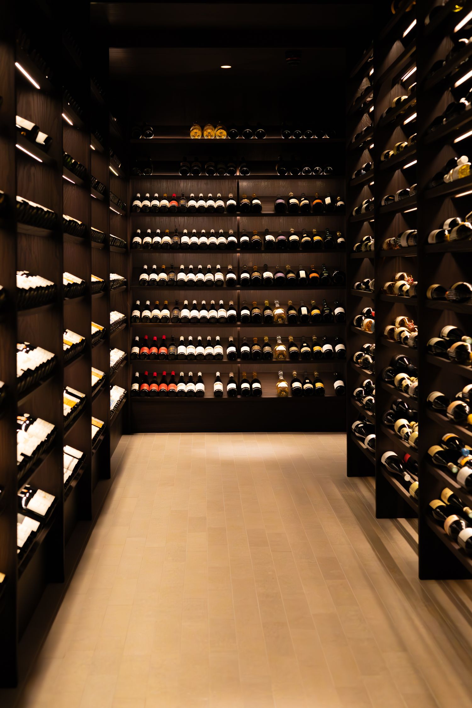 Elegant wine cellar interior with dark wood racks displaying organized wine bottles along illuminated walls.