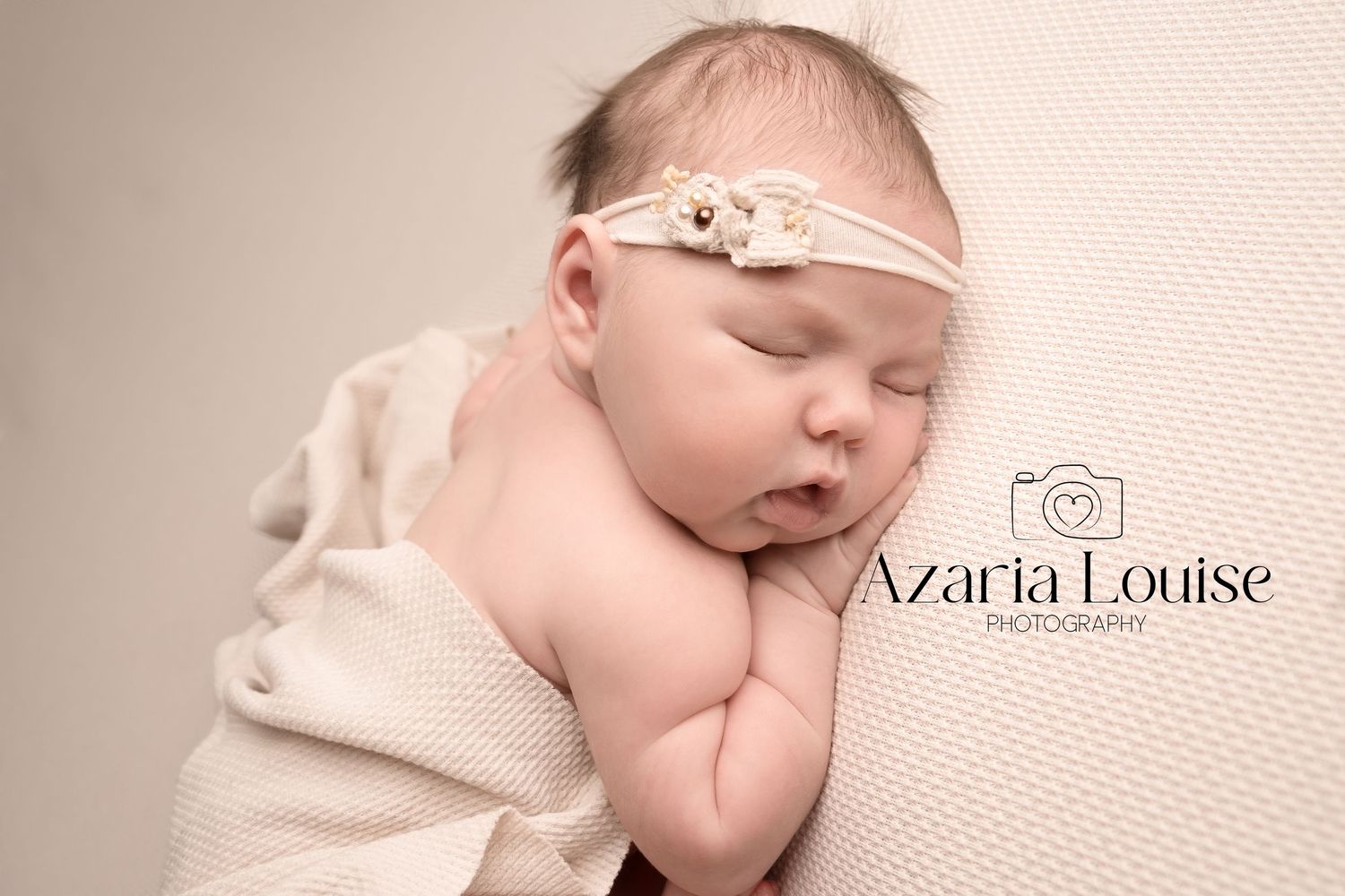 Sleeping newborn swaddled in cream fabric wearing delicate lace headband during professional photoshoot.