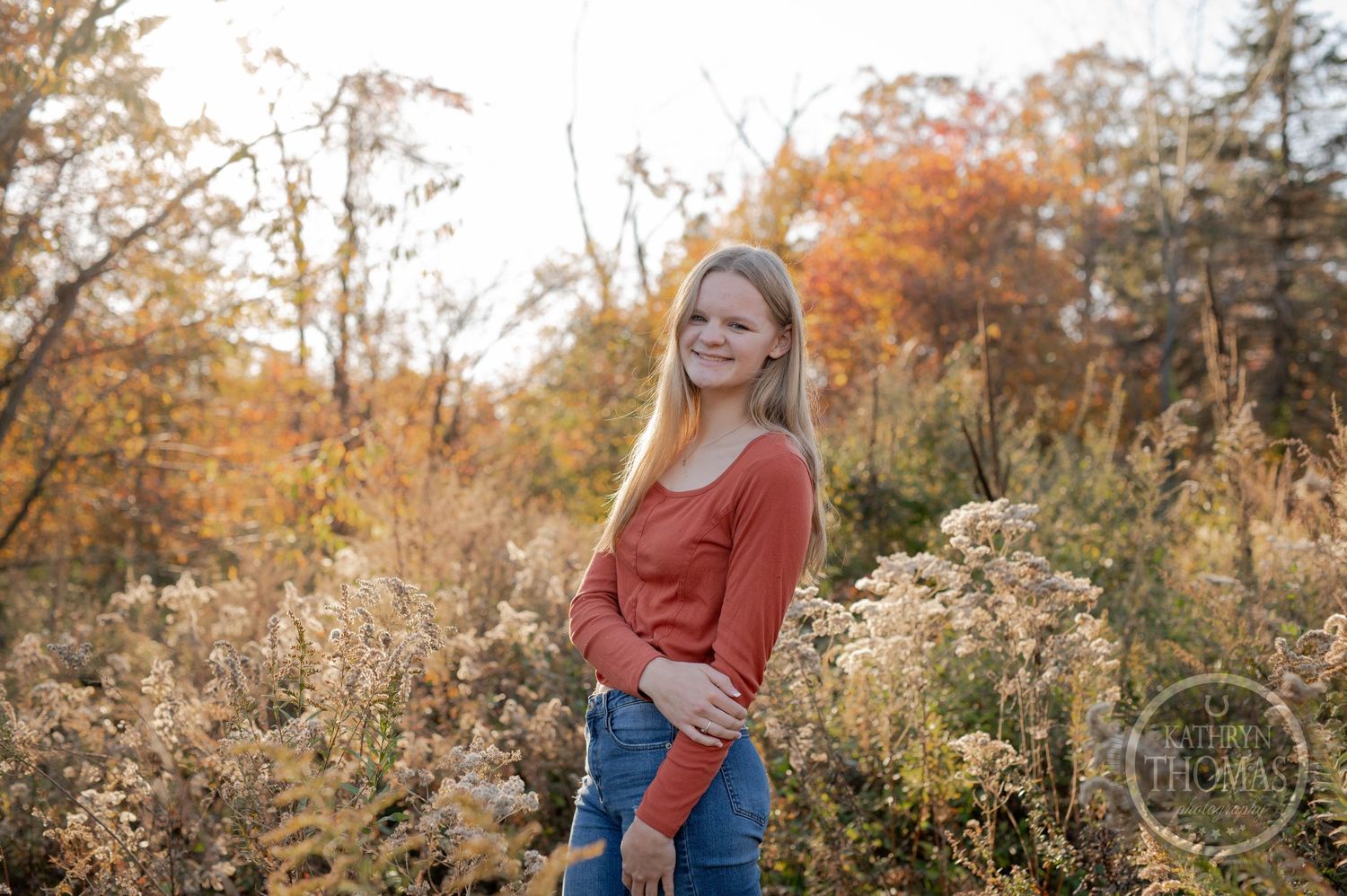 A warm autumn portrait featuring someone in a coral sweater against vibrant fall foliage.