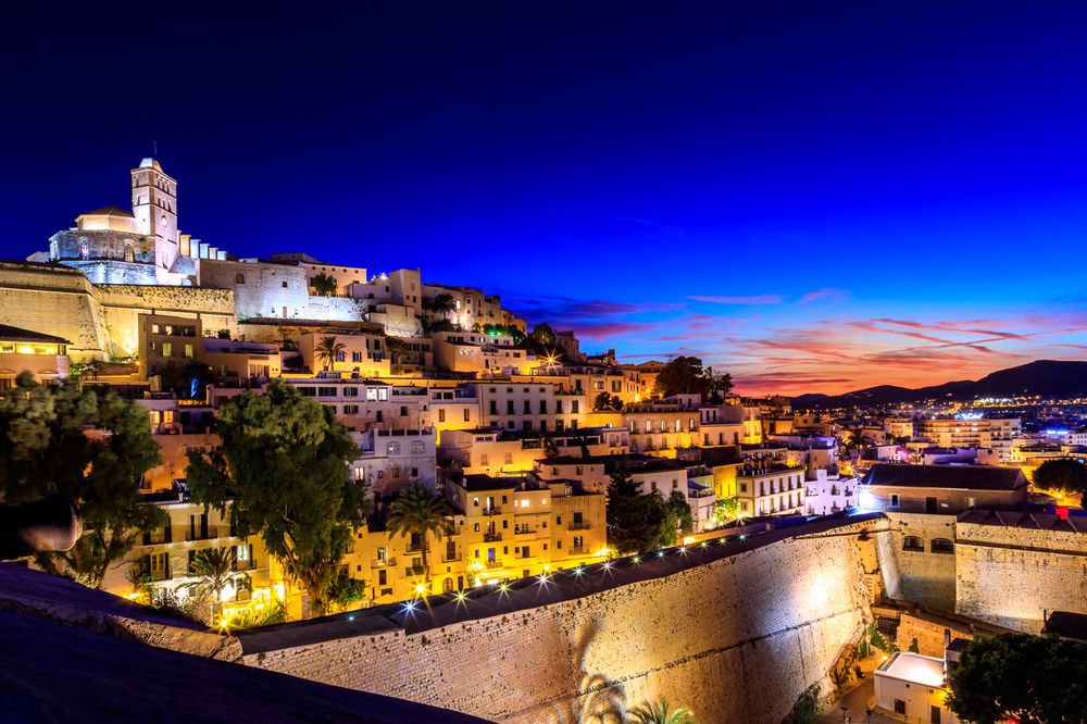 Ibiza Old Town Dalt Vila illuminated at dusk with ancient fortress walls and historic buildings overlooking the harbor.