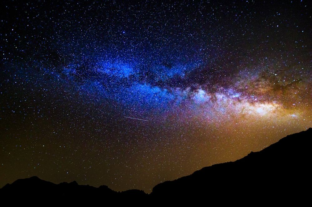 Silhouette of mountains against a starry night sky with the glowing Milky Way galaxy arching overhead.