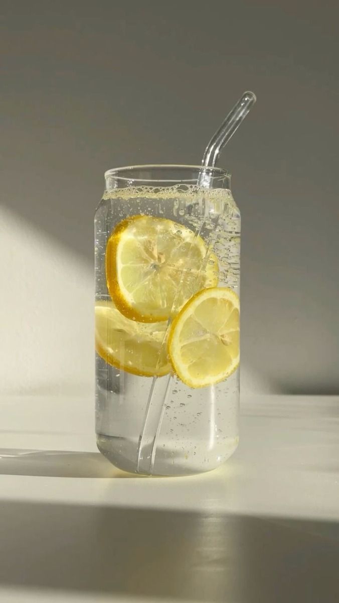 A glass of sparkling water with fresh lemon slices and ice cubes captured in a minimalist style against a light background.