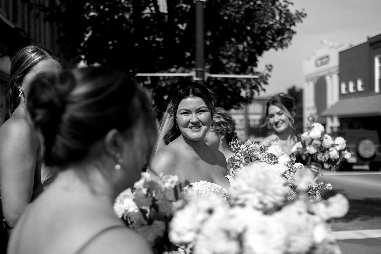 A bride wearing a lace dress and veil holding gorgeous florals smiles at her bridesmaids while walking to her wedding ceremony in Michigan.