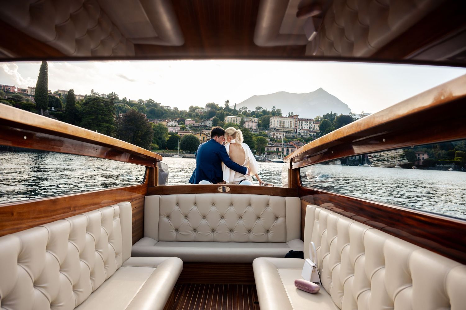 A luxury wooden boat with cream tufted leather seating cruises along a scenic mountain lake.