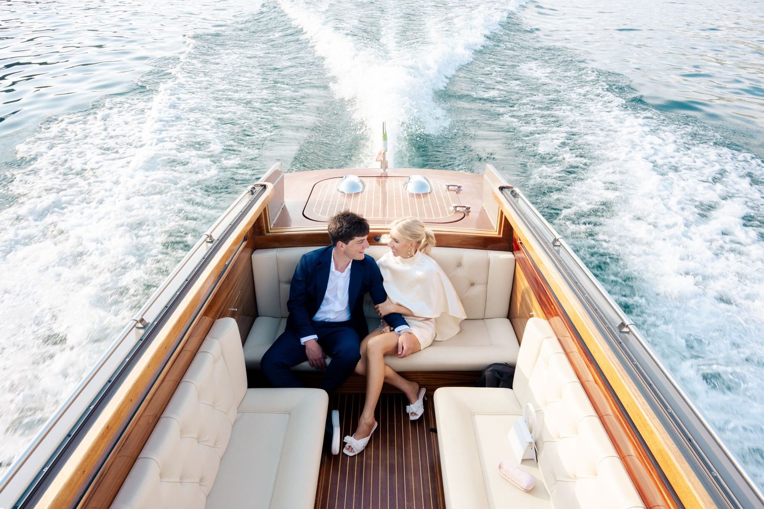 A luxury wooden boat cruises through blue waters leaving a white wake trail behind it.