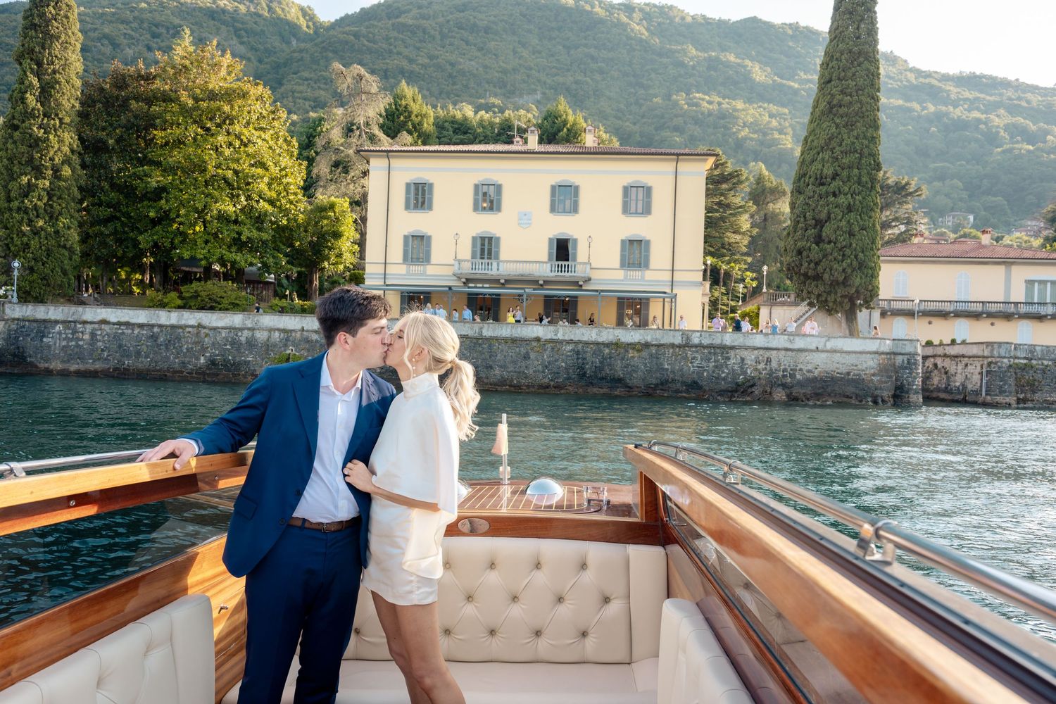 Couple enjoying a romantic boat ride along Lake Como's scenic shoreline with historic Italian villas in the background.