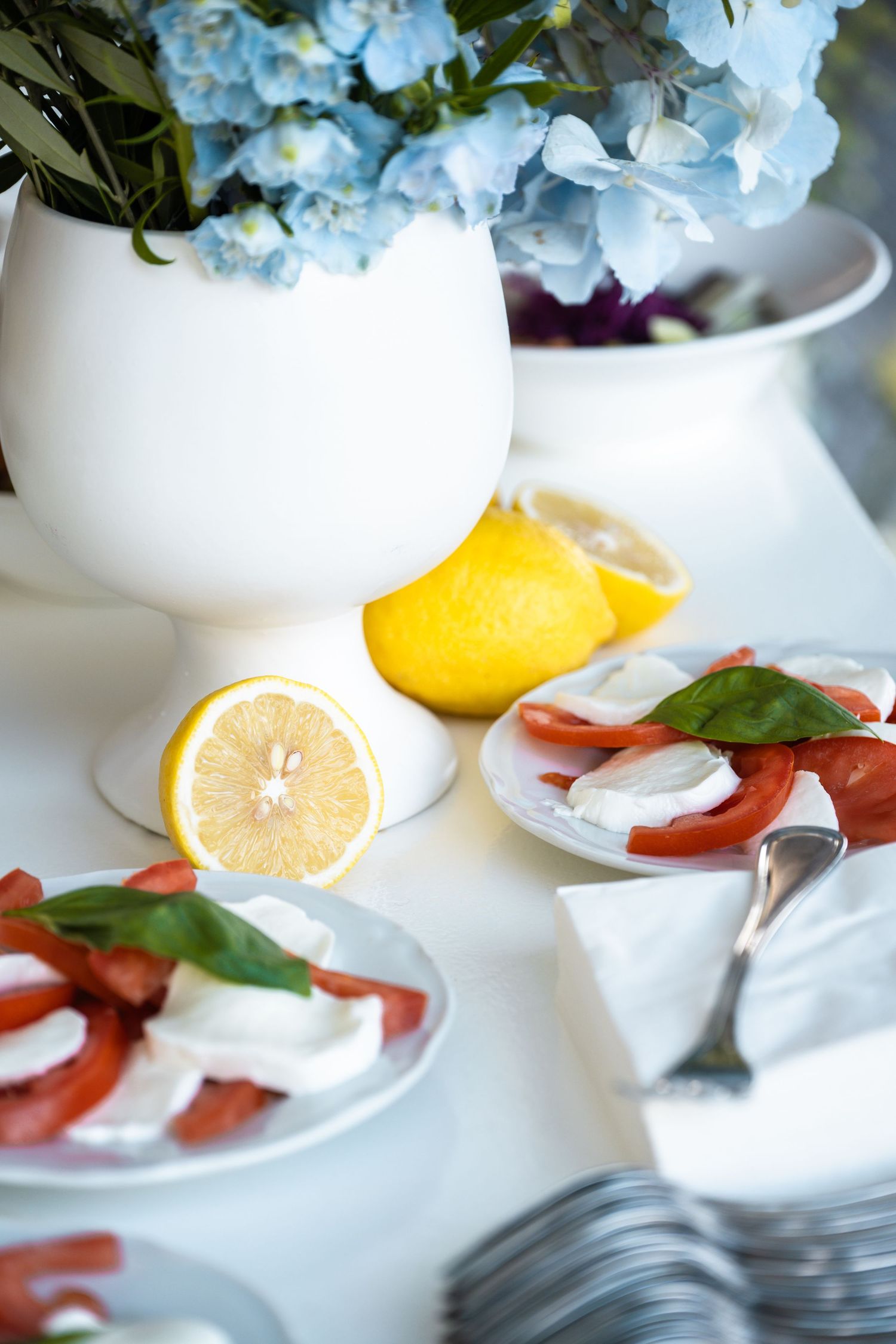 Fresh lemon slices and delicate blue hydrangea flowers create an elegant table setting with white porcelain dishes.