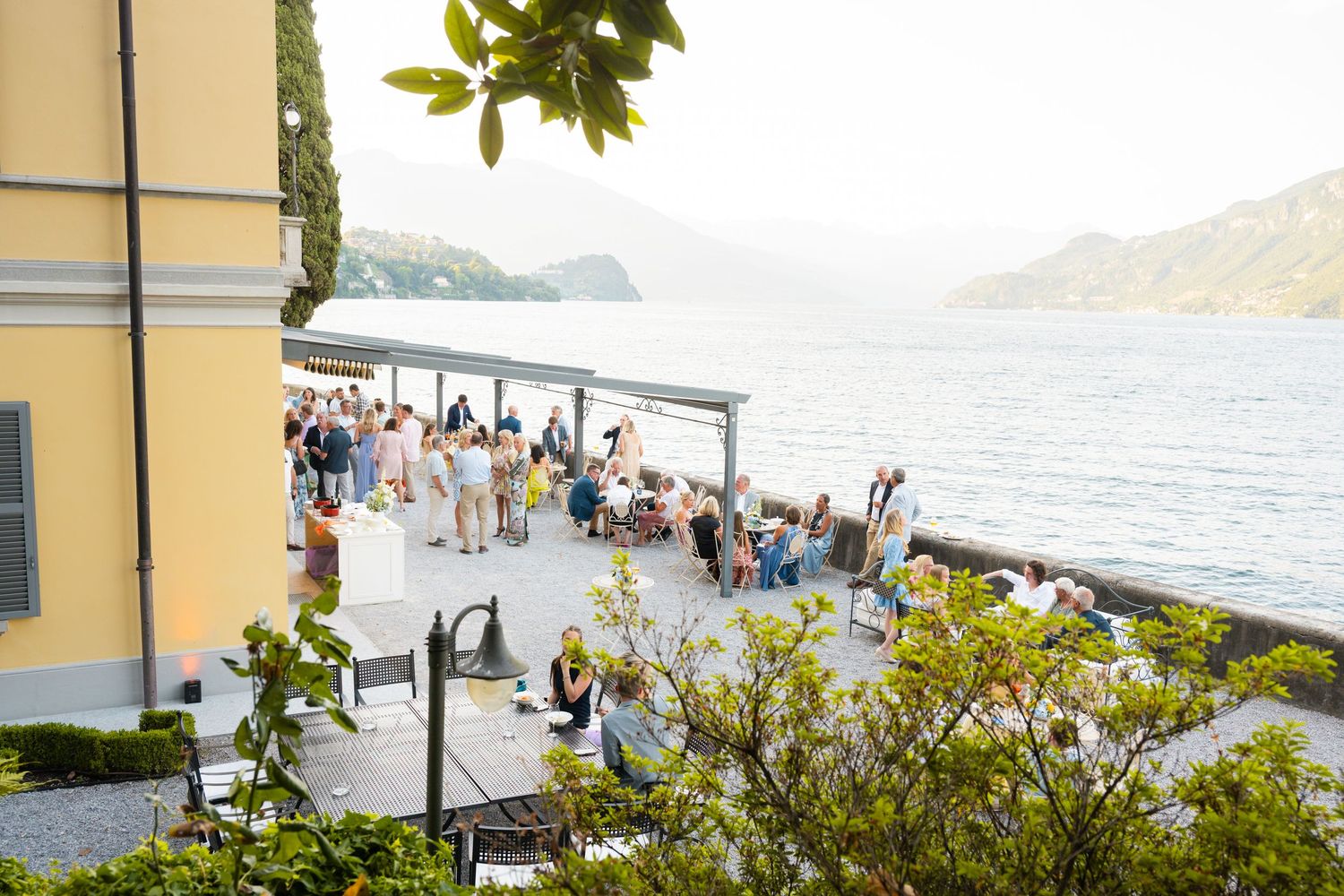 Scenic coastal pathway with yellow buildings and lush greenery overlooking a beautiful Mediterranean bay on a sunny day.