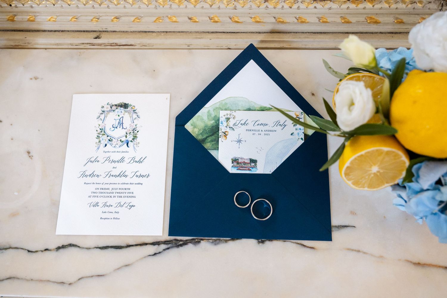 Wedding invitation suite with navy blue envelopes, rings, and delicate blue floral accents displayed on a light surface.