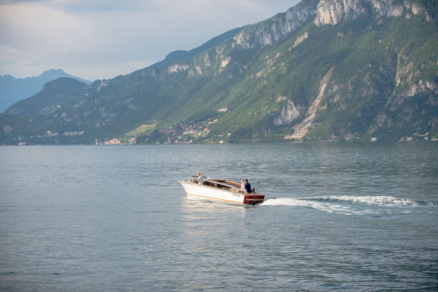 A speedboat cruises across a scenic mountain lake surrounded by steep cliffs and green hillsides.