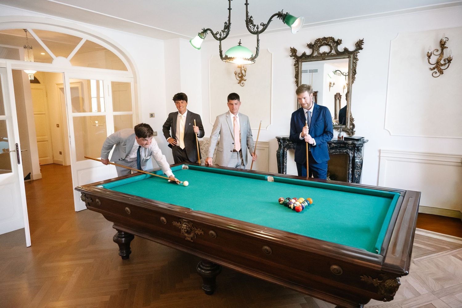 People enjoying a game of billiards in an elegant white-walled room with multiple pool tables and classic decor.
