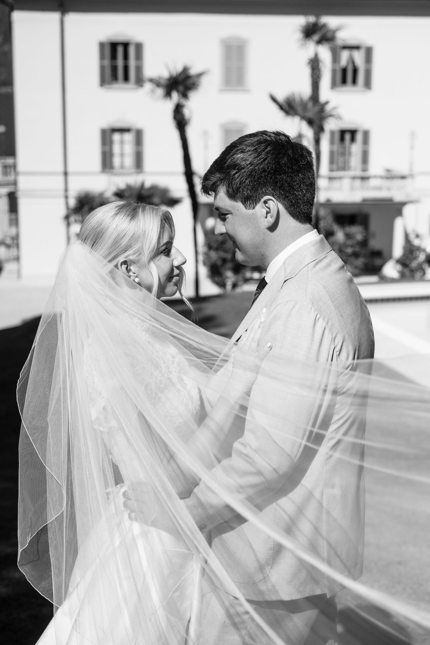 Black and white wedding photo sequence showing a couple embracing under flowing white veil in romantic moment.