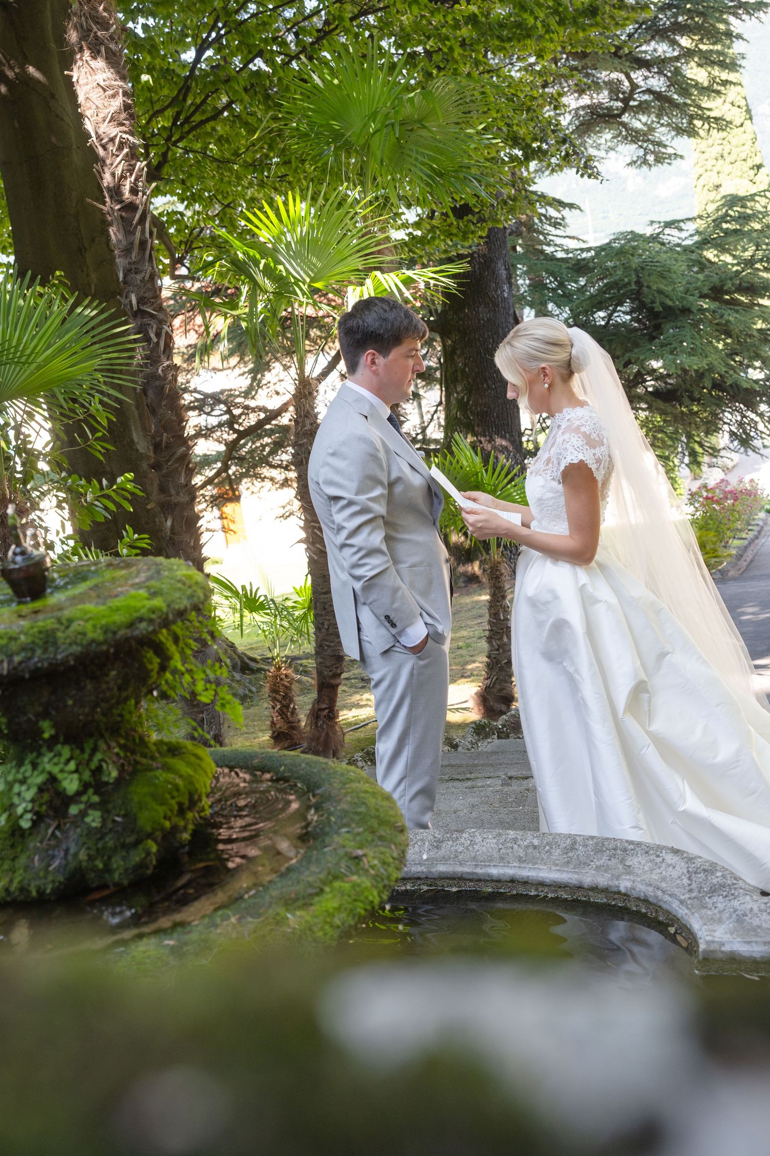 A couple shares an intimate moment in a lush garden setting with palm trees and greenery creating a romantic backdrop.