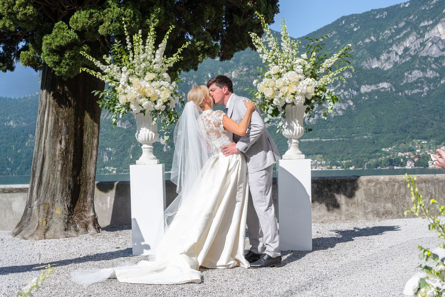 Elegant outdoor wedding ceremony with white floral arrangements and mountain backdrop at Lake Como, Italy.