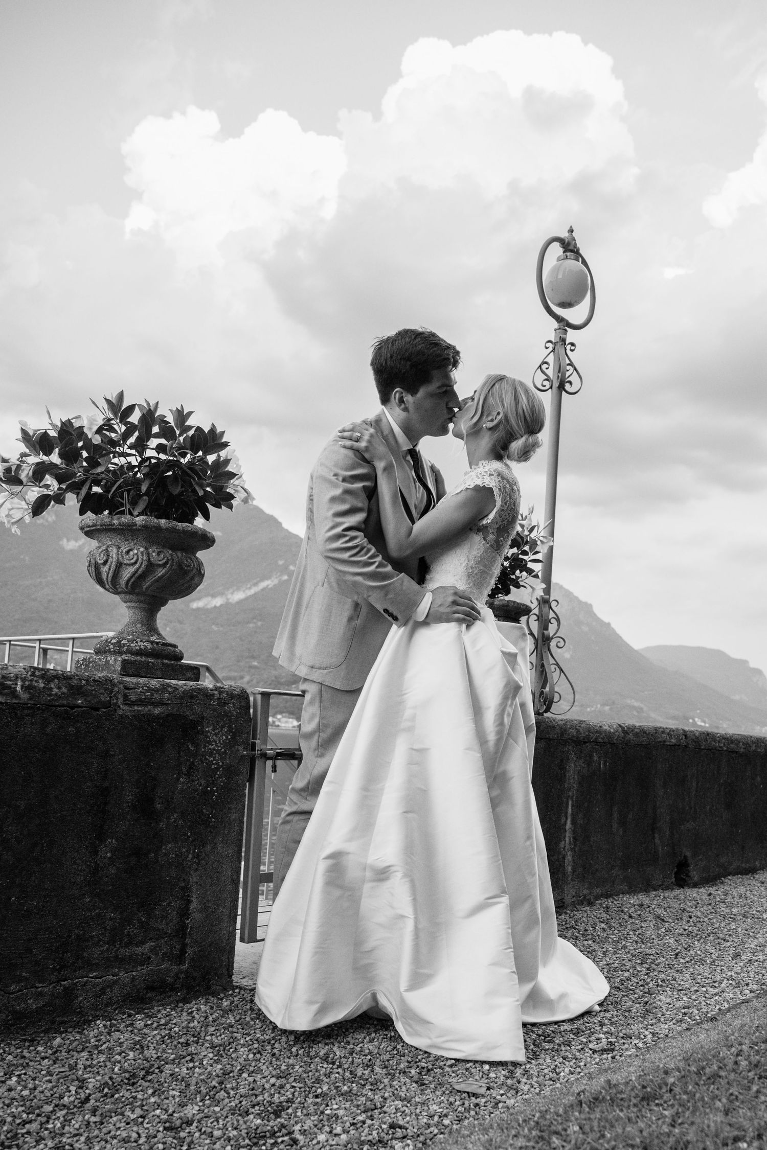 Romantic black and white wedding photo of a couple embracing on a terrace overlooking mountains in Italy.