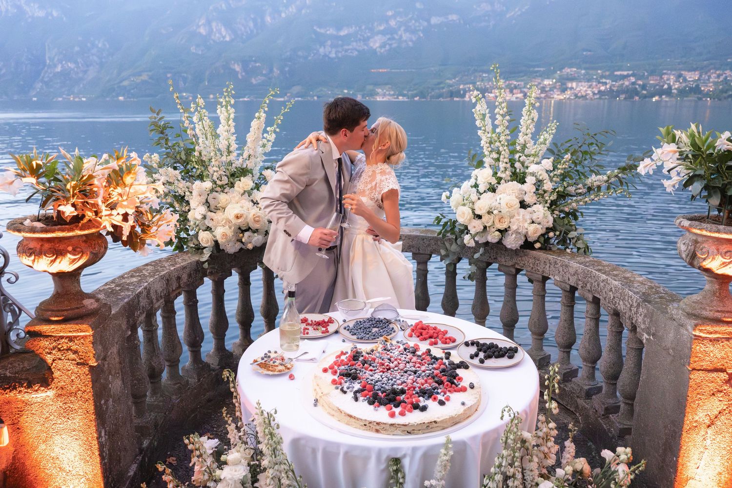 Elegant wedding reception tables with floral centerpieces overlooking Lake Como from a stone balcony terrace in Italy.