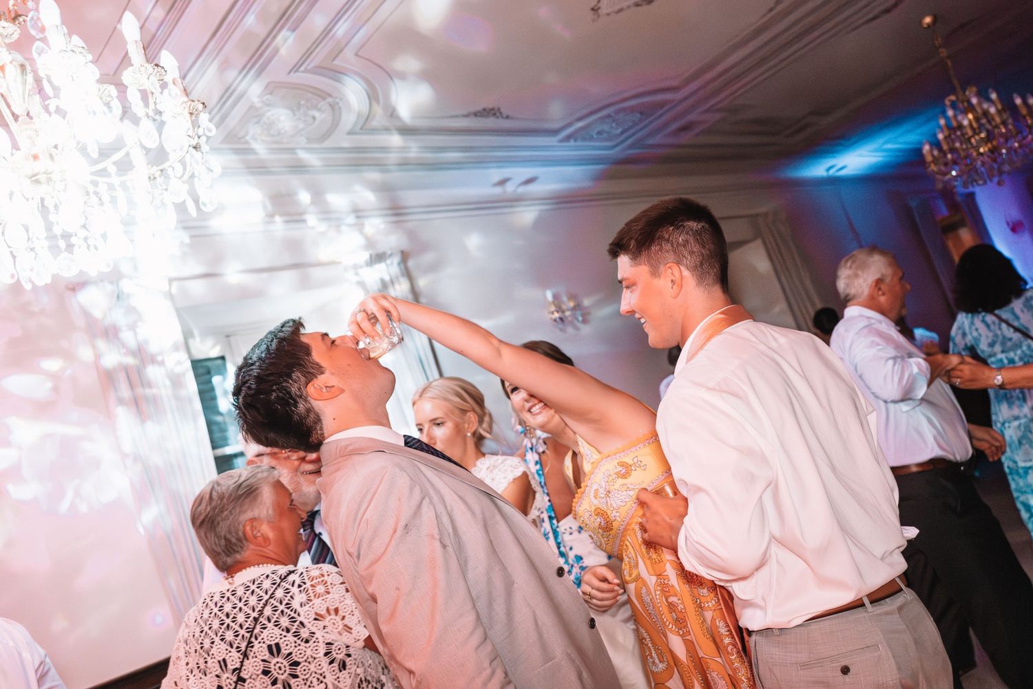 Guests enjoying a celebration on a dance floor with blue and pink lighting effects in an indoor venue.
