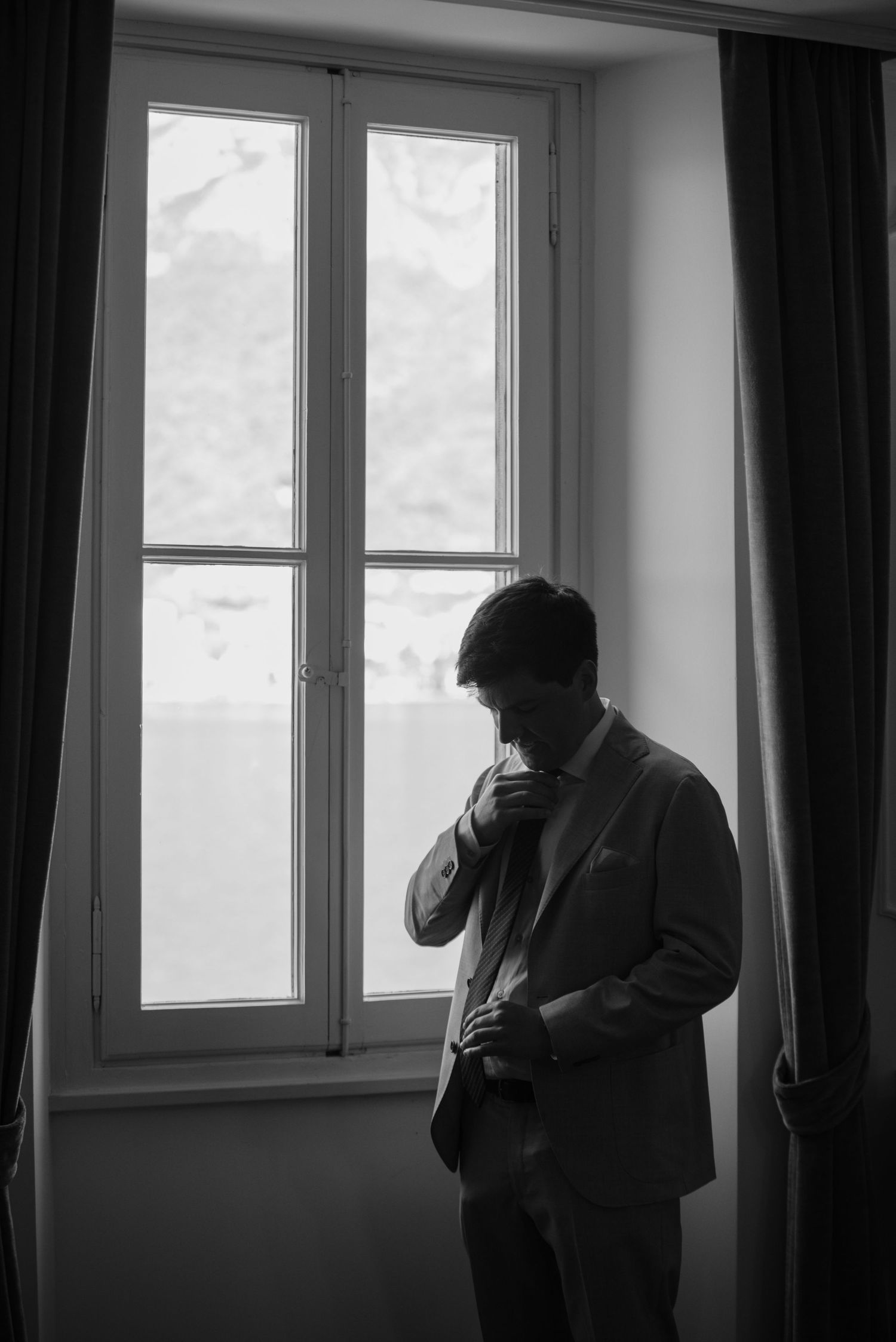 A silhouetted figure stands near windows in a dark room creating a moody black and white composition.