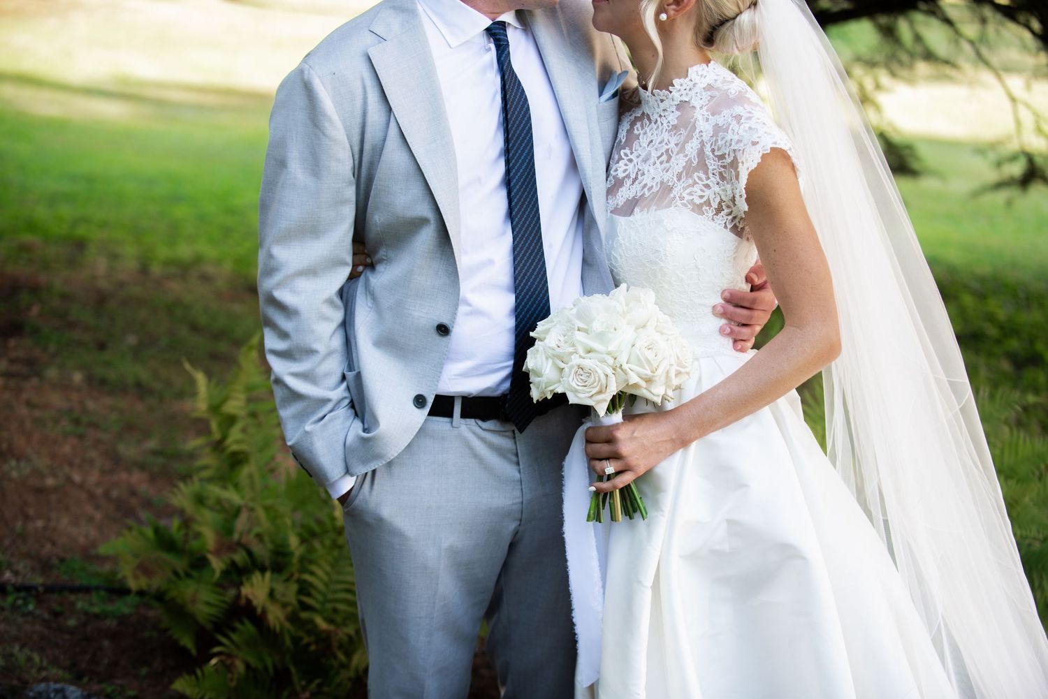 A couple in wedding attire poses together outdoors in a garden setting during their special day.