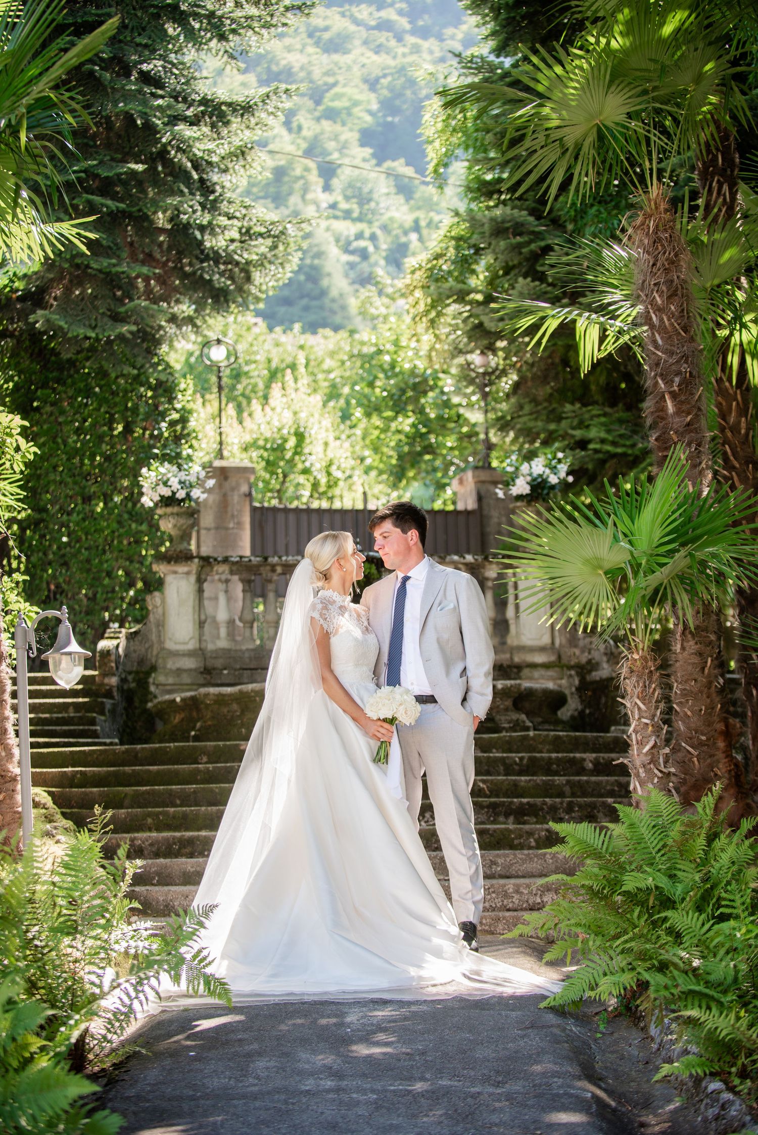 A romantic wedding photo series in a lush garden setting with stone steps and tropical palm trees.