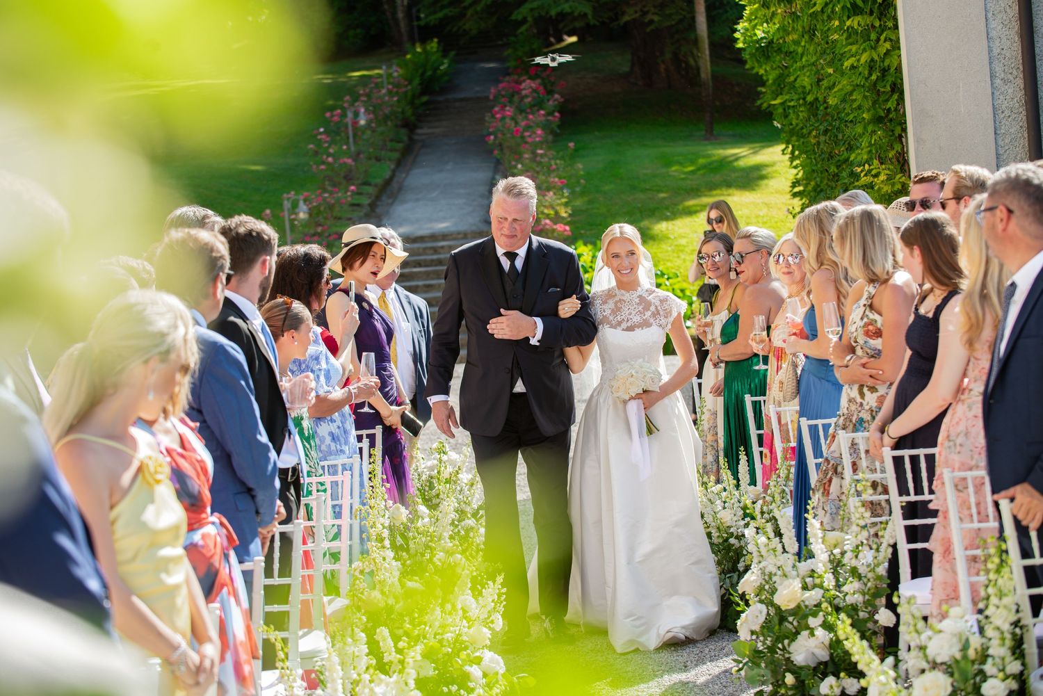 A wedding party gathers outdoors in a garden setting for a joyful summer celebration.