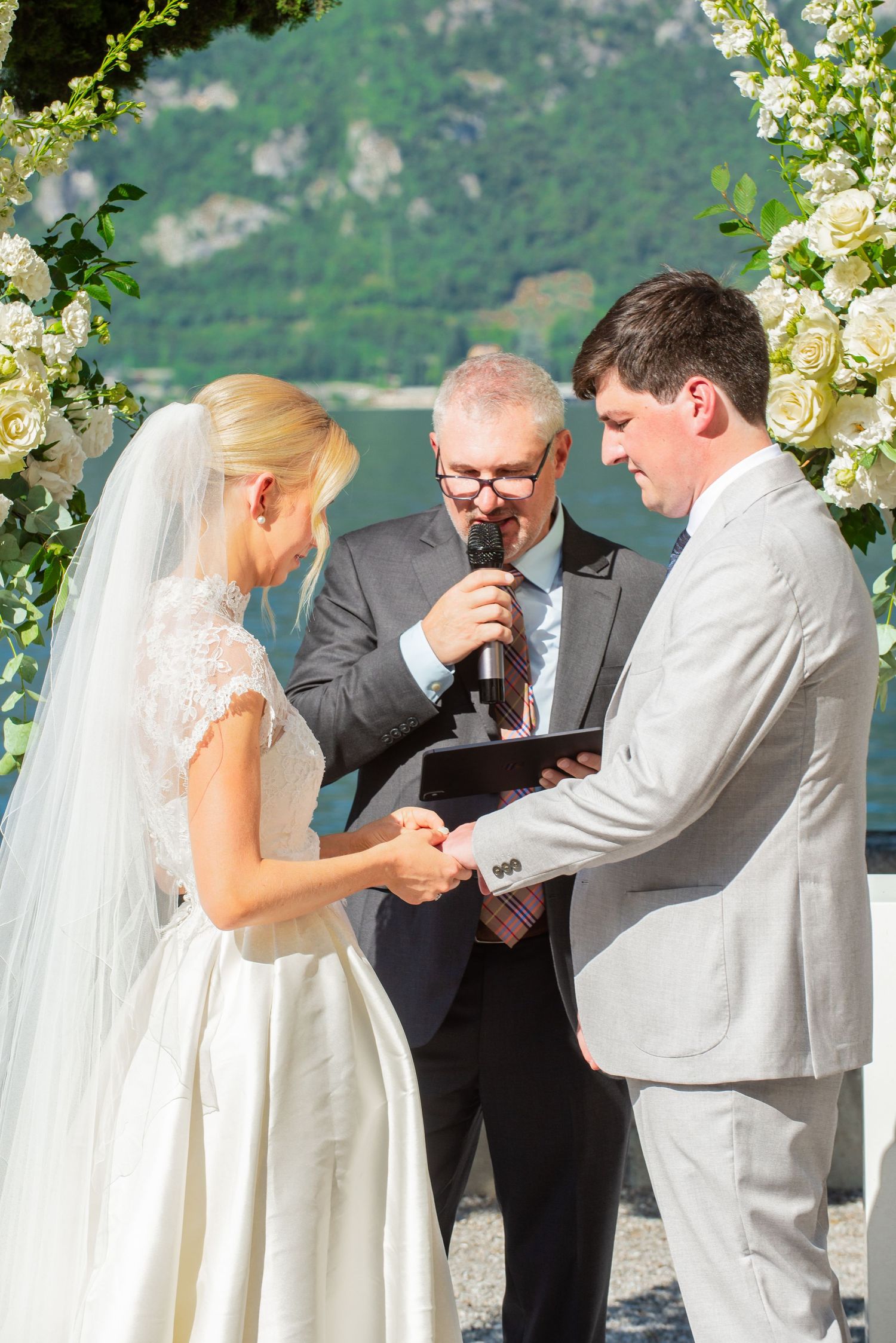 Wedding ceremony sequence shows couple exchanging rings with officiant under floral arch against mountain backdrop.