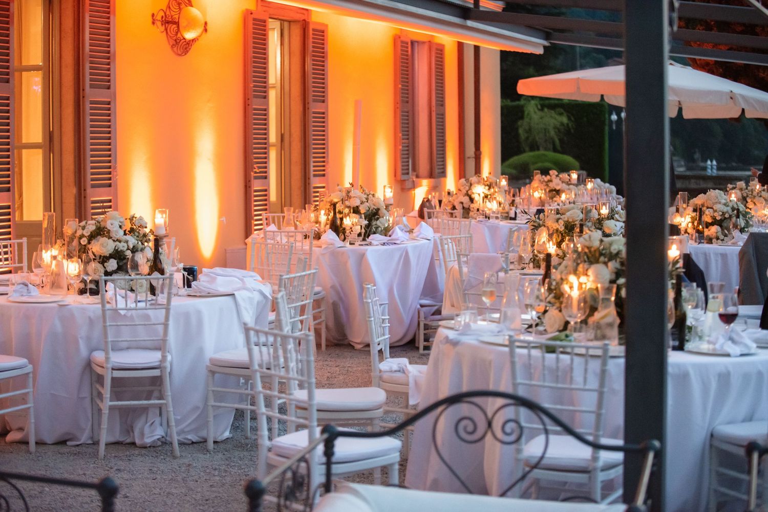 Elegant wedding reception venue with white tables, floral centerpieces, and warm amber lighting creating a romantic atmosphere.