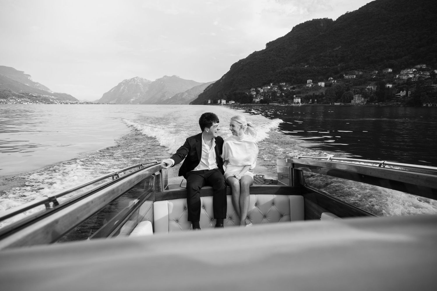 A couple sits together in a boat on a scenic mountain lake with misty peaks in the background.