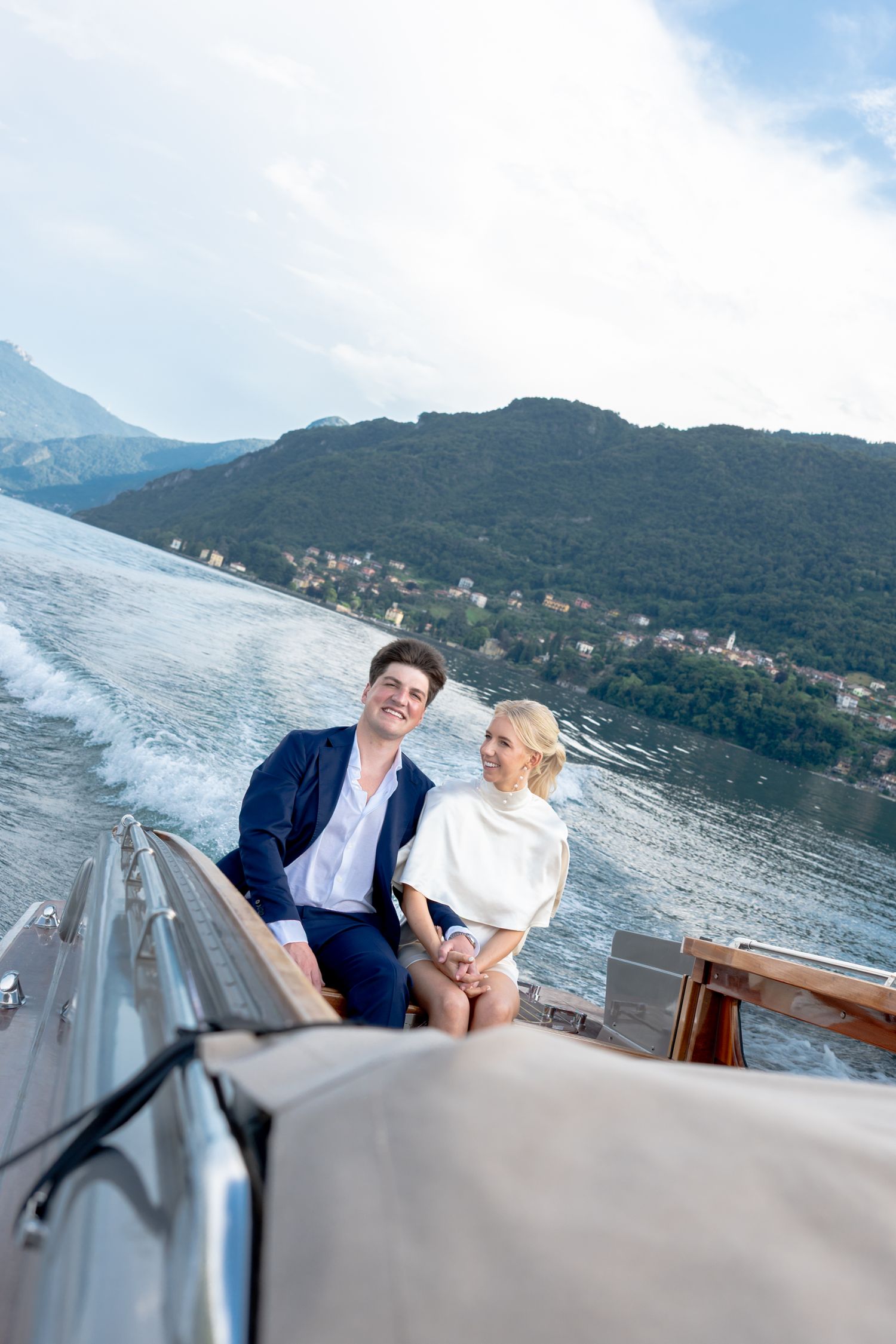 Couple enjoying a scenic boat ride along Lake Como with mountains and coastal villages in the background.